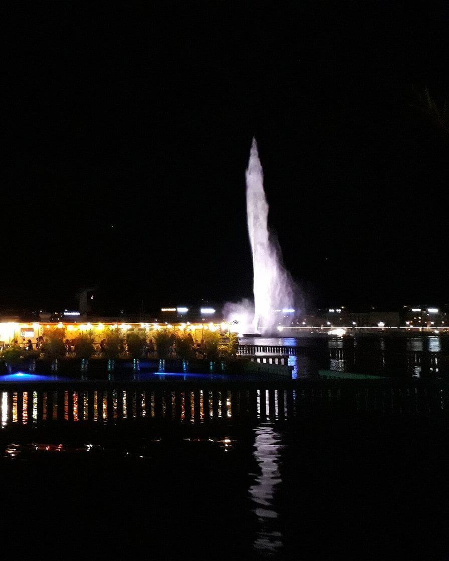 Tische der Buvette der Bains des Pâquis auf dem Steg im Genfersee, mit Blick auf die Bucht und den Jet d'eau, an einem Winterabend