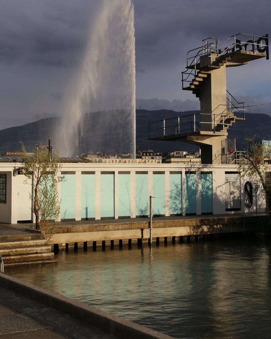 Le plongeoir des Bains des Pâquis à Genève, avec un baigneur qui saute dans le lac Léman et la rade derrière