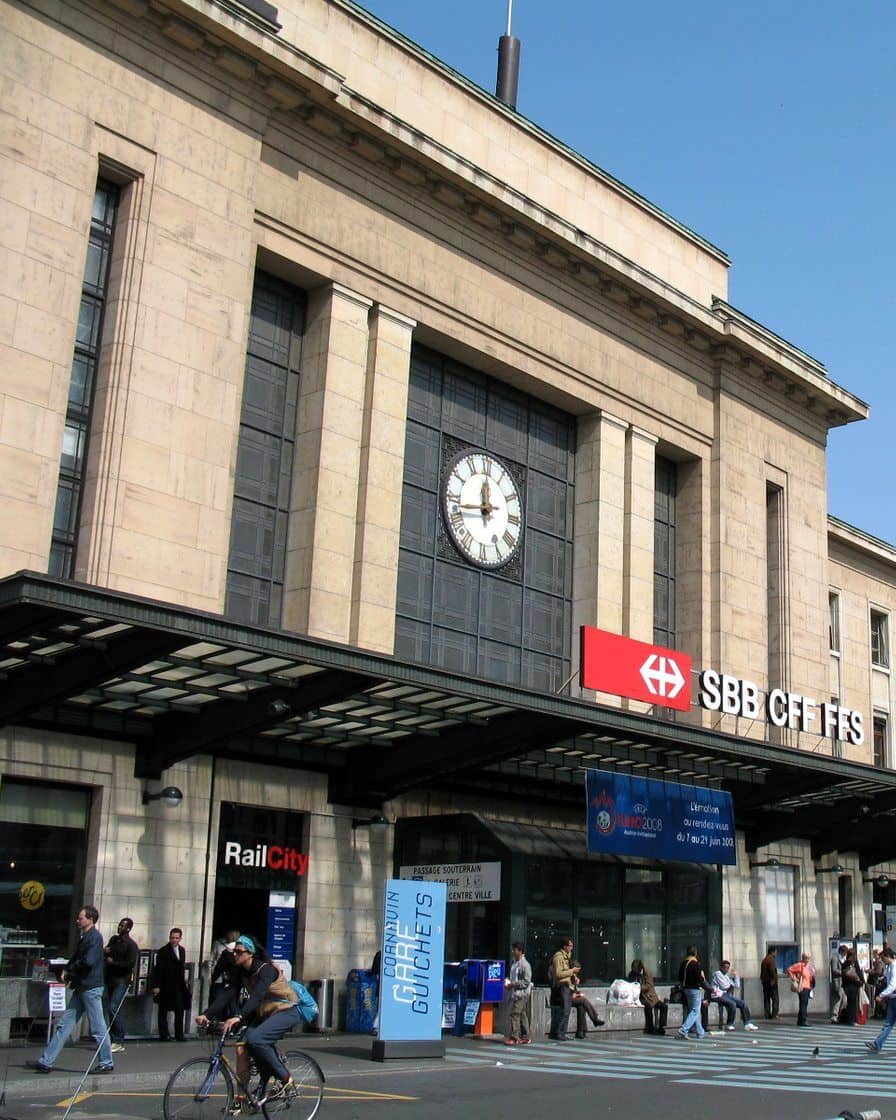 Façade of Genève-Cornavin station on Place de Cornavin, with a tram and passengers in front of the main entrance