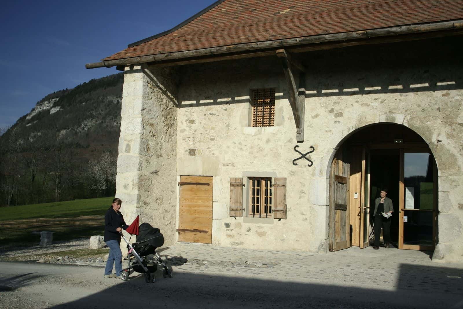 La Maison du Salève, ancienne ferme en pierre au pied de la montagne, avec des visiteurs devant l'entrée