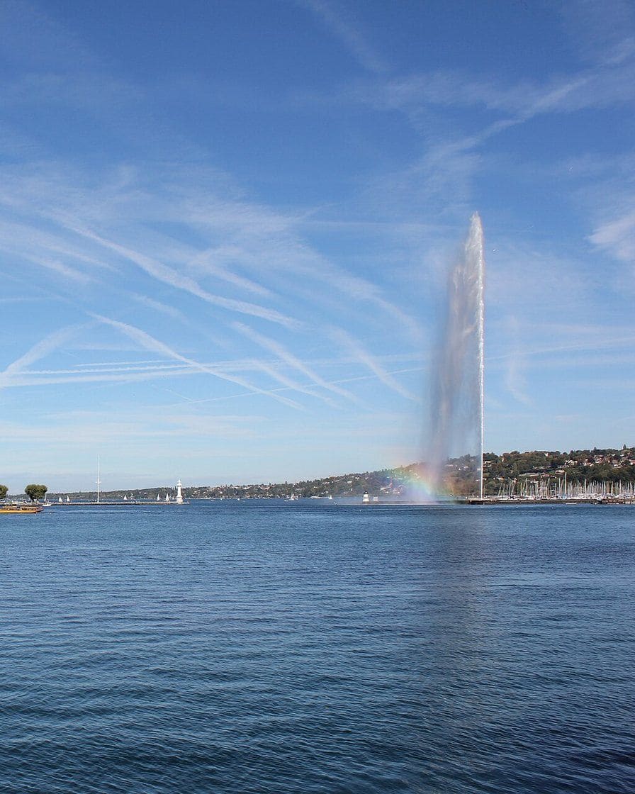 La rada de Ginebra vista desde el puente del Mont-Blanc, el Jet d'eau, los muelles y el Salève a lo lejos con cielo despejado