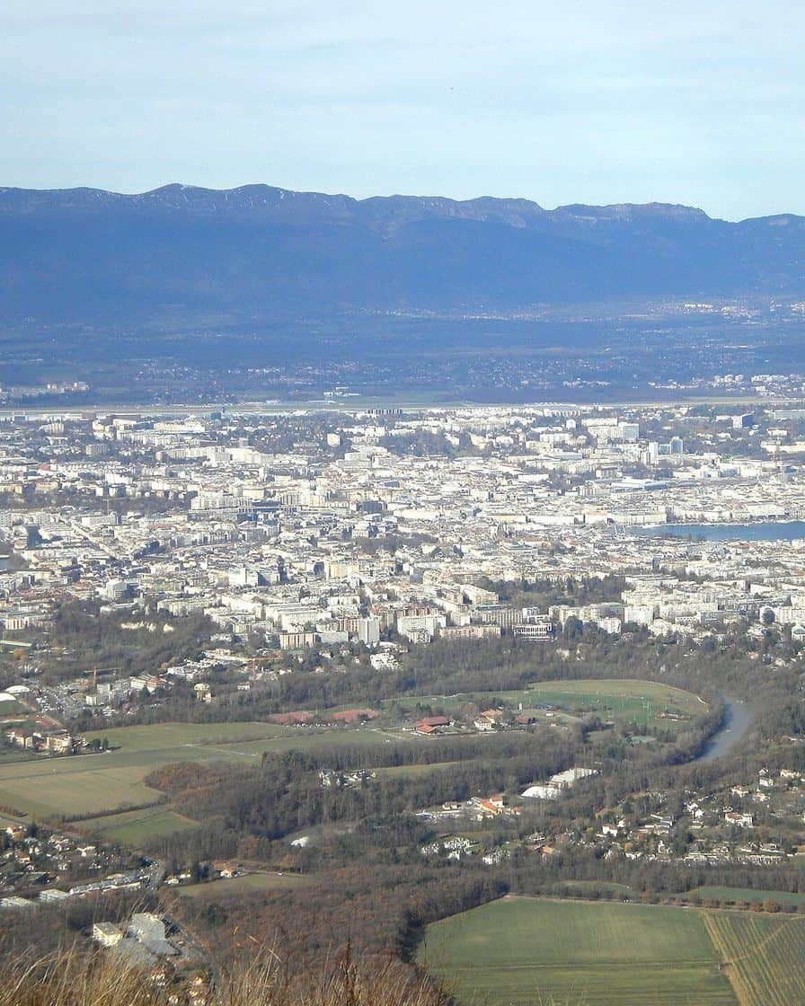 La cabine rouge du téléphérique du Salève suspendue au-dessus de la falaise calcaire, avec Genève et le lac Léman en contrebas